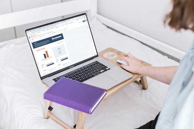 person using a laptop on their bed to manage their finances